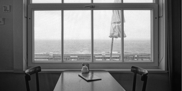 Blick durch ein verregnetes Fenster auf das Meer über eienen Tisch hinweg